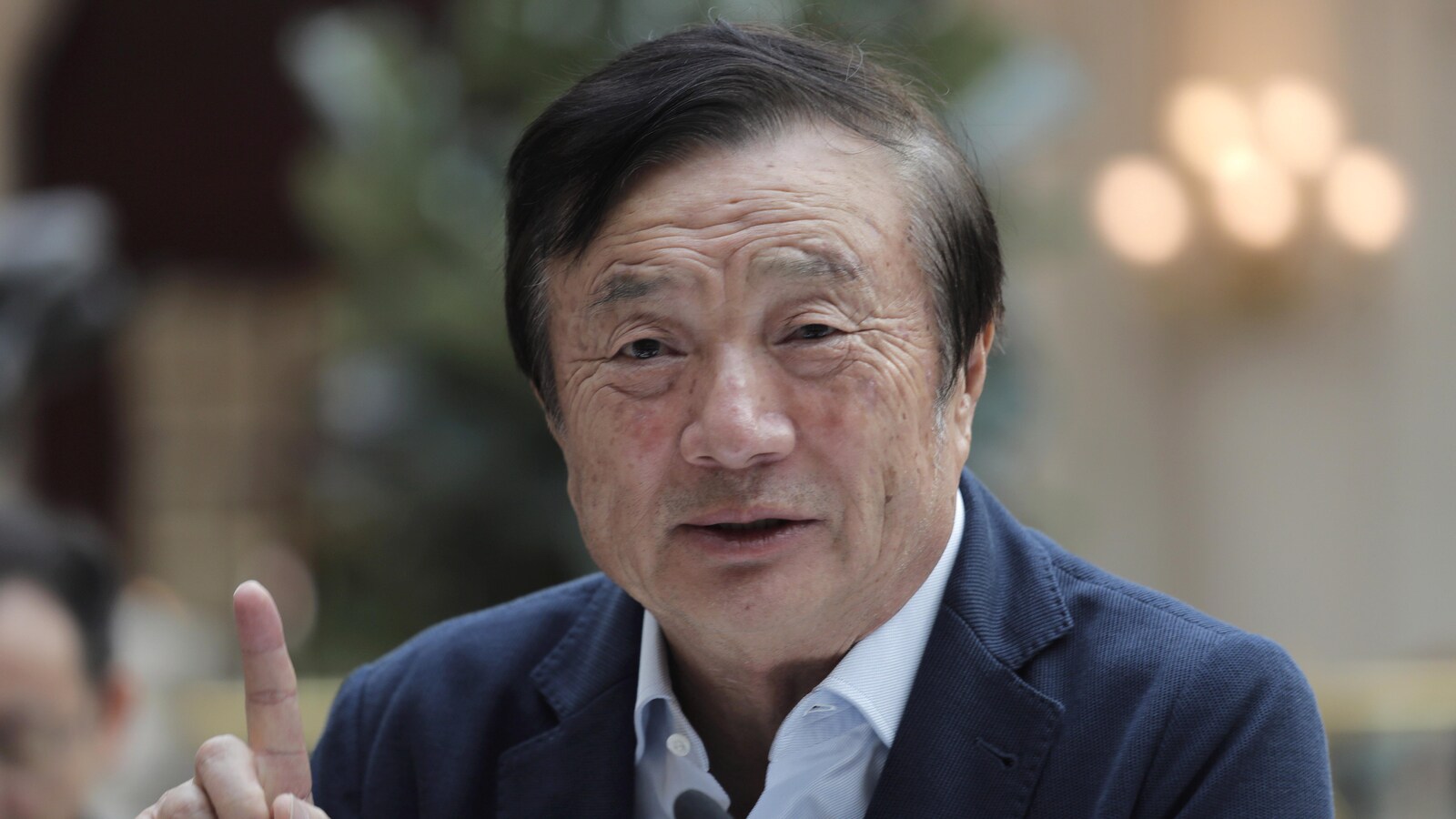 Ren Zhengfei, devant un micro, lève le doigt.