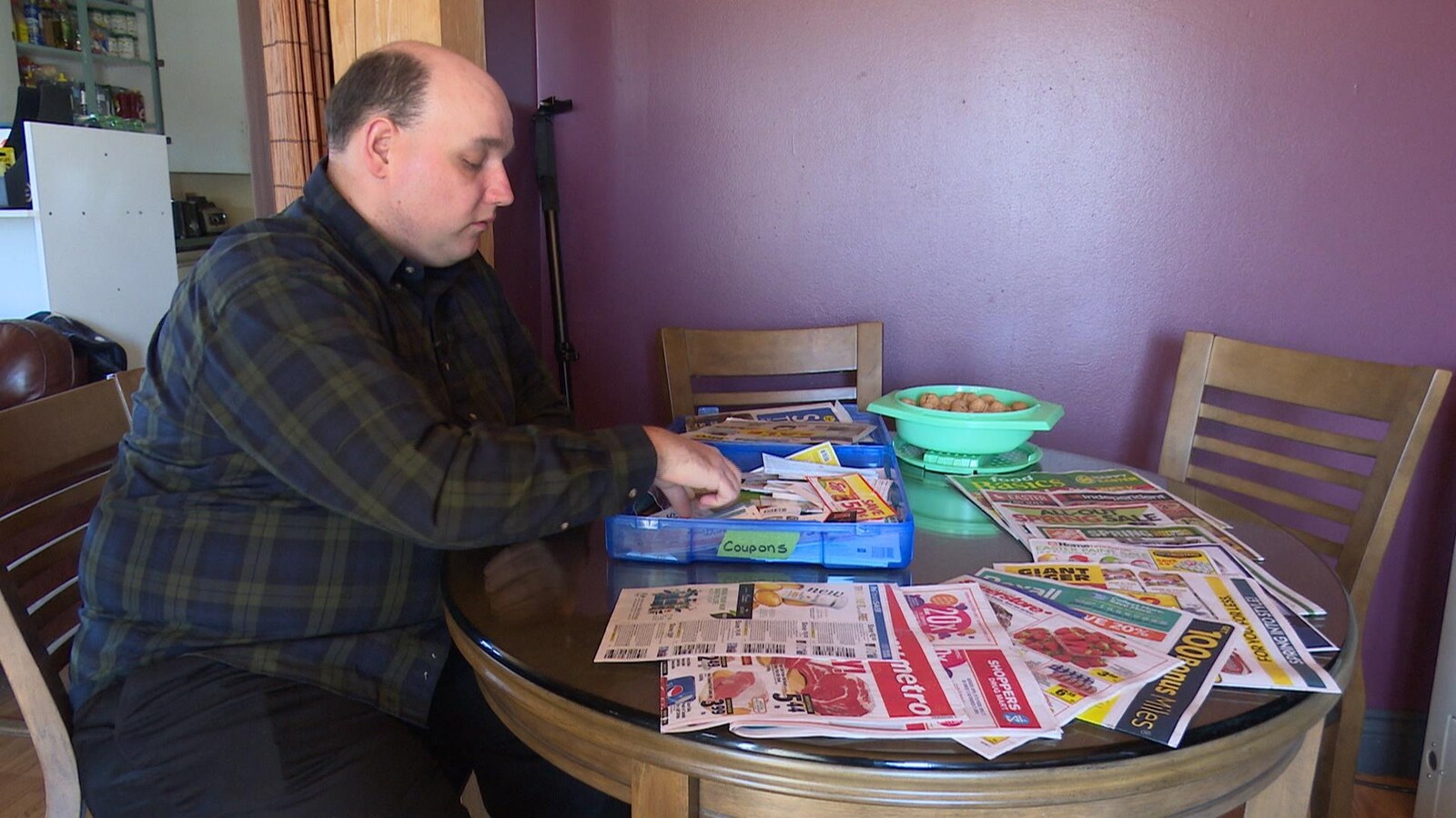 Charles Tossell parcourt des coupons de rabais, assis à sa table.