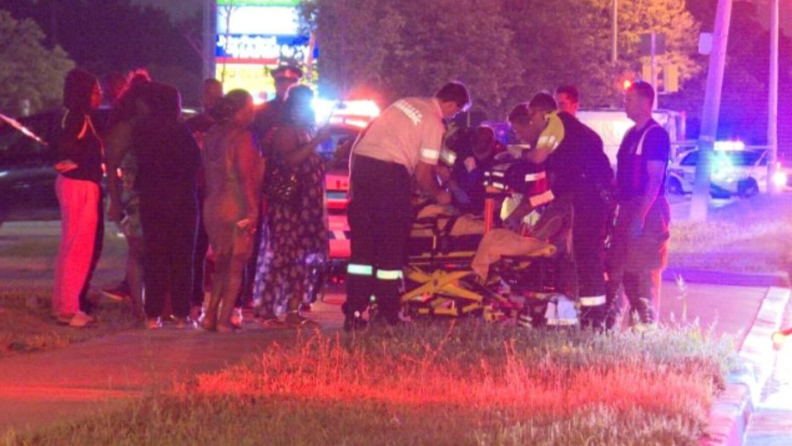 Des ambulanciers tentent de porter secours à un homme atteint par balles, il est sur un brancard, caché par les urgentistes, il fait nuit et quelques personnes se trouvent autour.