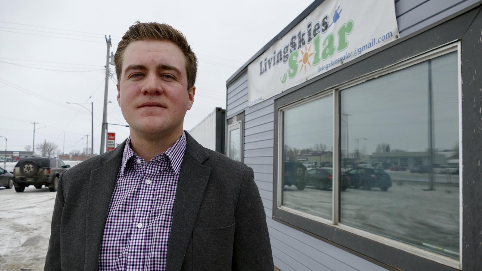 Un homme, debout devant l'entrée d'une petite entreprise. Un panneau sur la façade derrière lui dit : "Living Skies Solar".