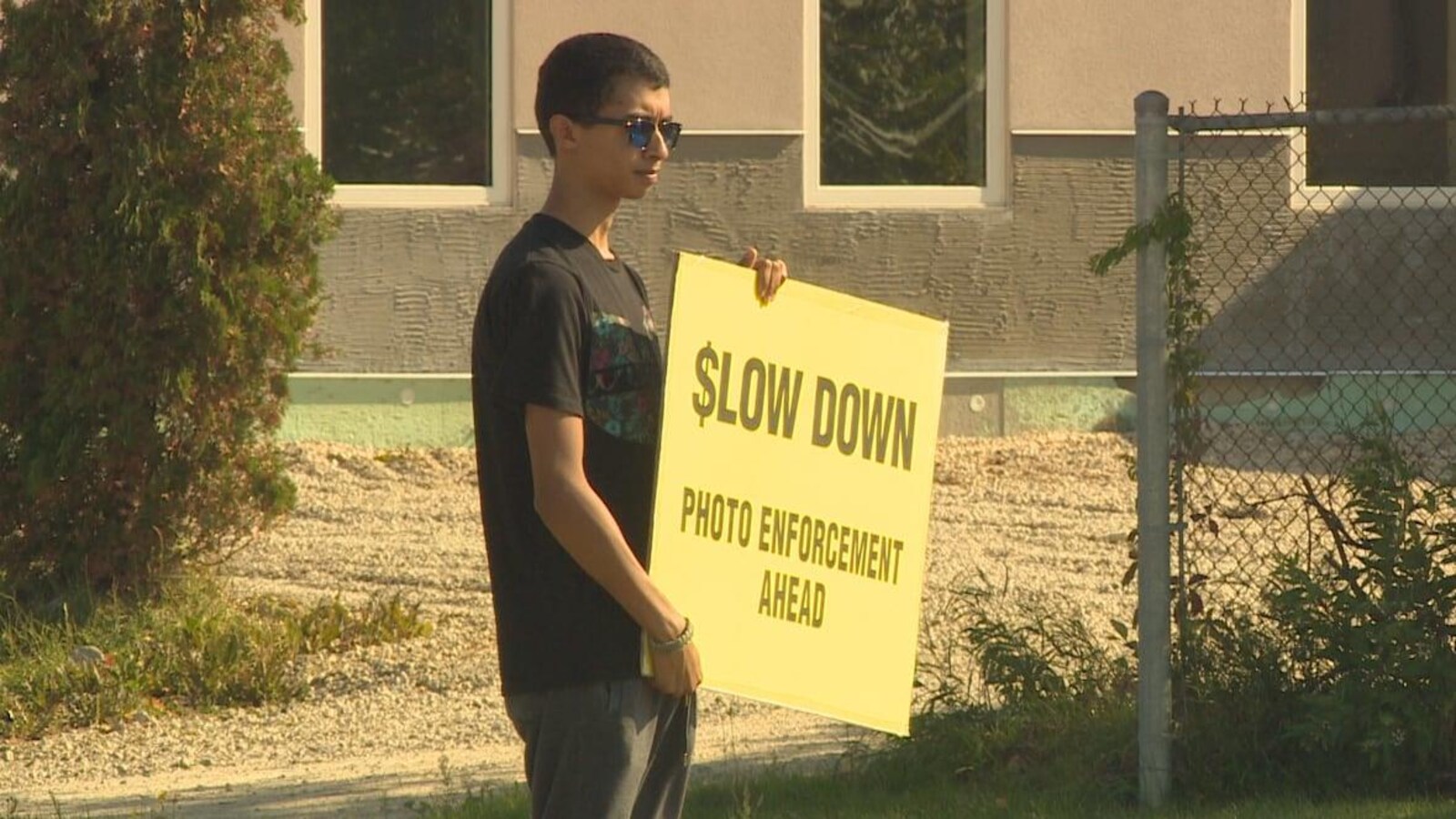 Un jeune homme tenant une affiche jaune sur laquelle on peut lire en anglais les mots : Ralentissez, radar photo devant.