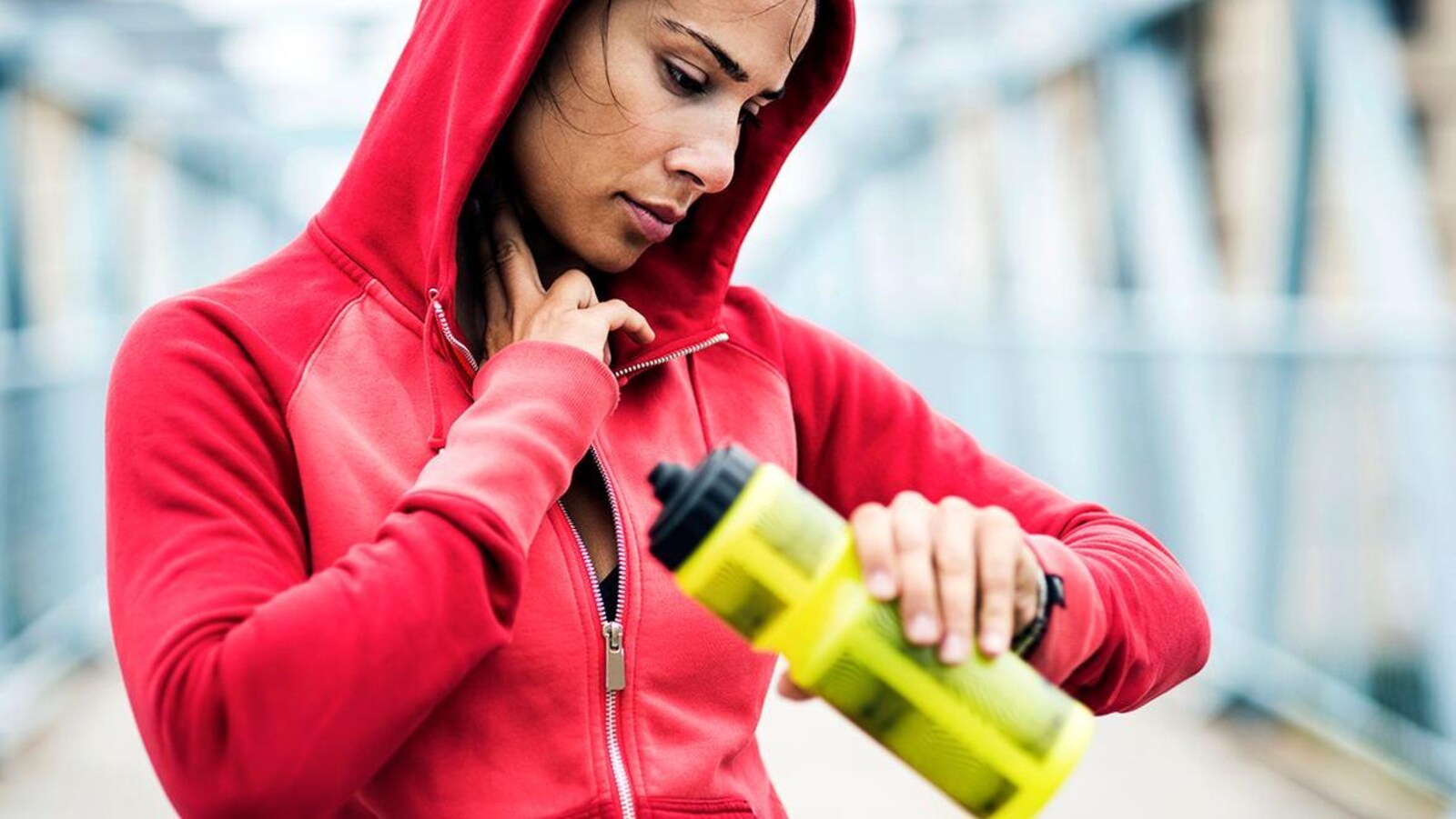 Une femme en train de faire de courir, s'arrête pour prendre son poux avec une bouteille d'eau jaune à la main.