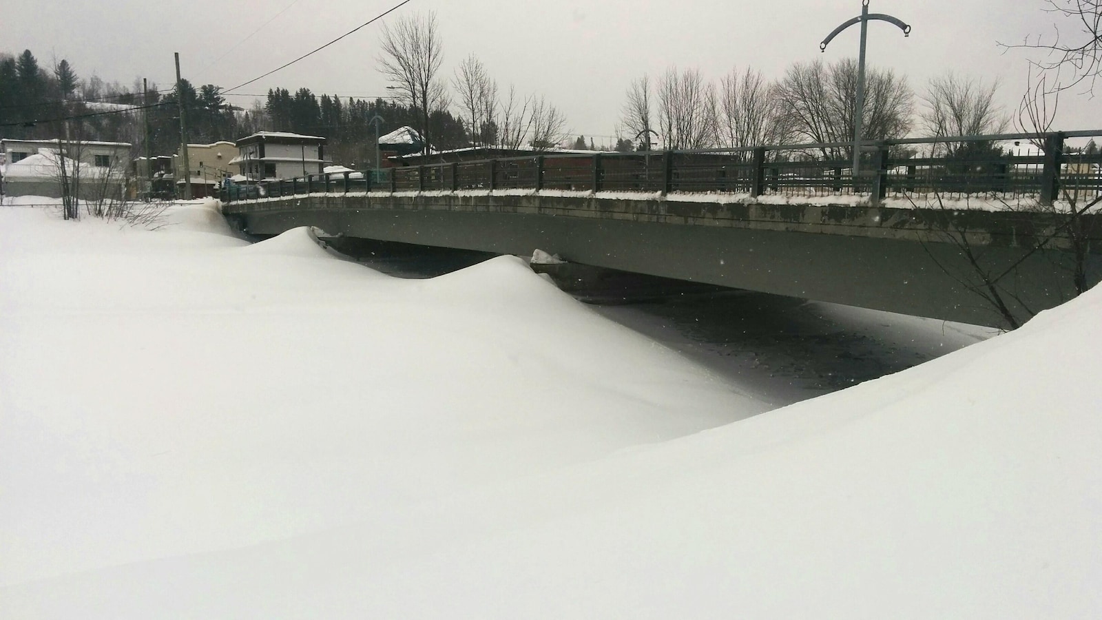 La rivière Sainte-Anne photographiée en hiver. On aperçoit un pont surplombant la rivière. Cette dernière est entièrement recouverte de neige.