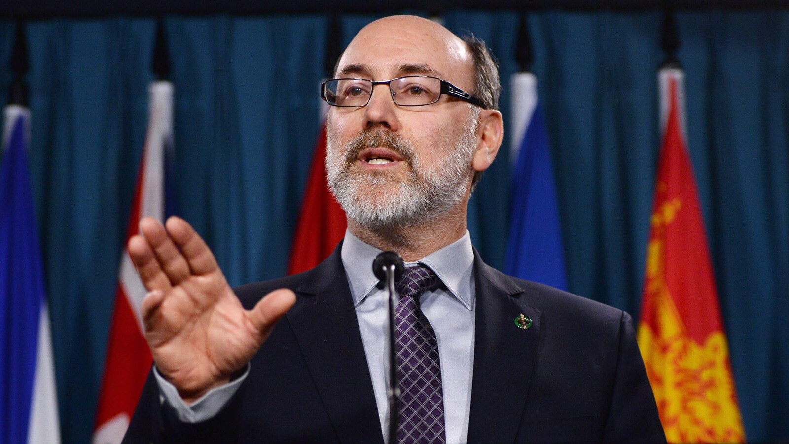 Robert Aubin au micro devant des drapeaux provinciaux