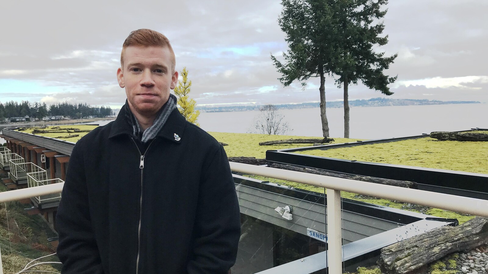 Un jeune homme avec un manteau sur le bord de l'eau.