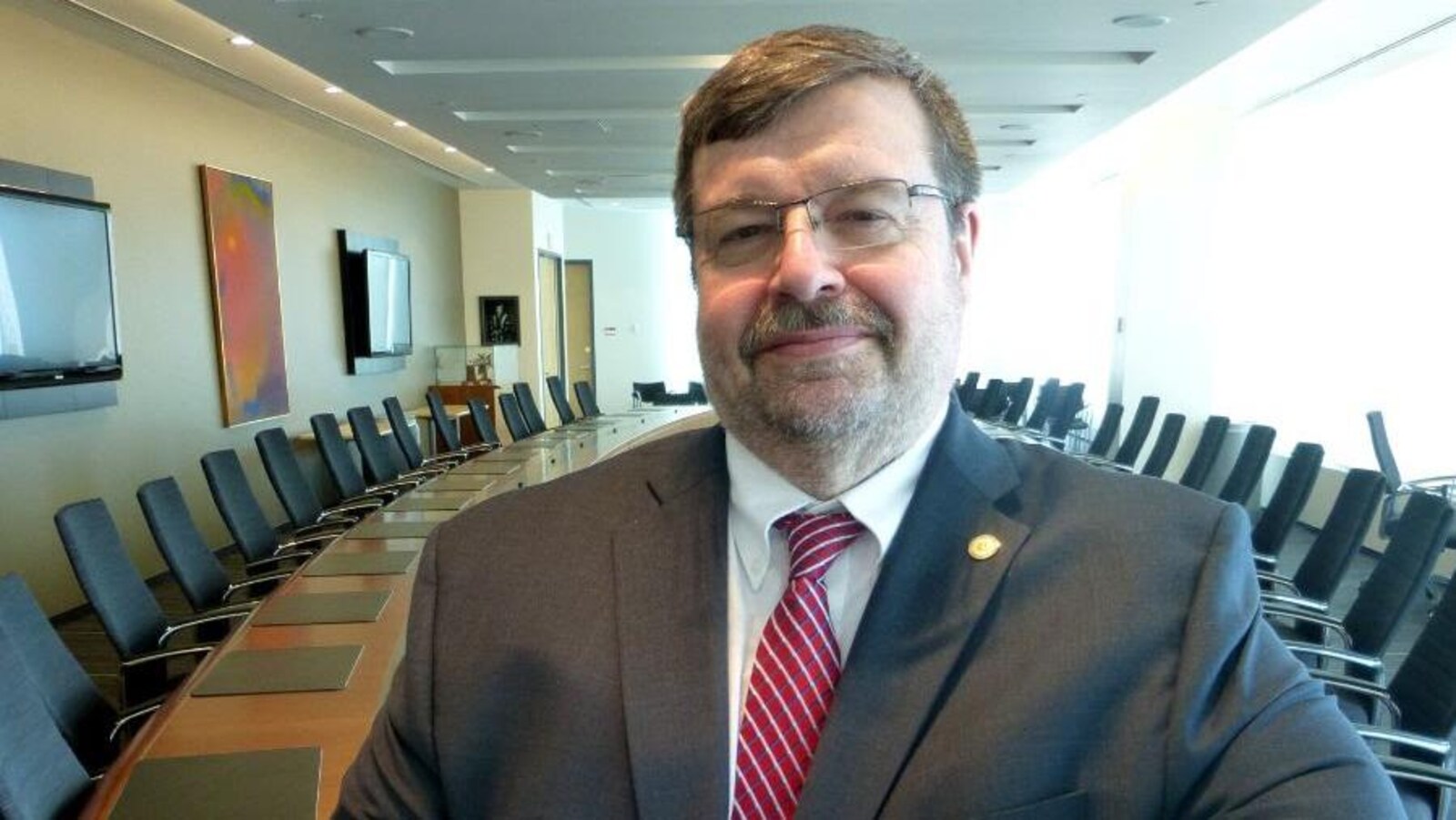 Robert Haché devant une grande table dans une salle de réunion