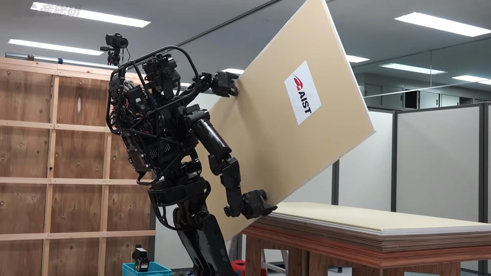 Une capture d'écran d'une vidéo montrant le robot HRP-5P en train de saisir une plaque de plâtre sur une table.