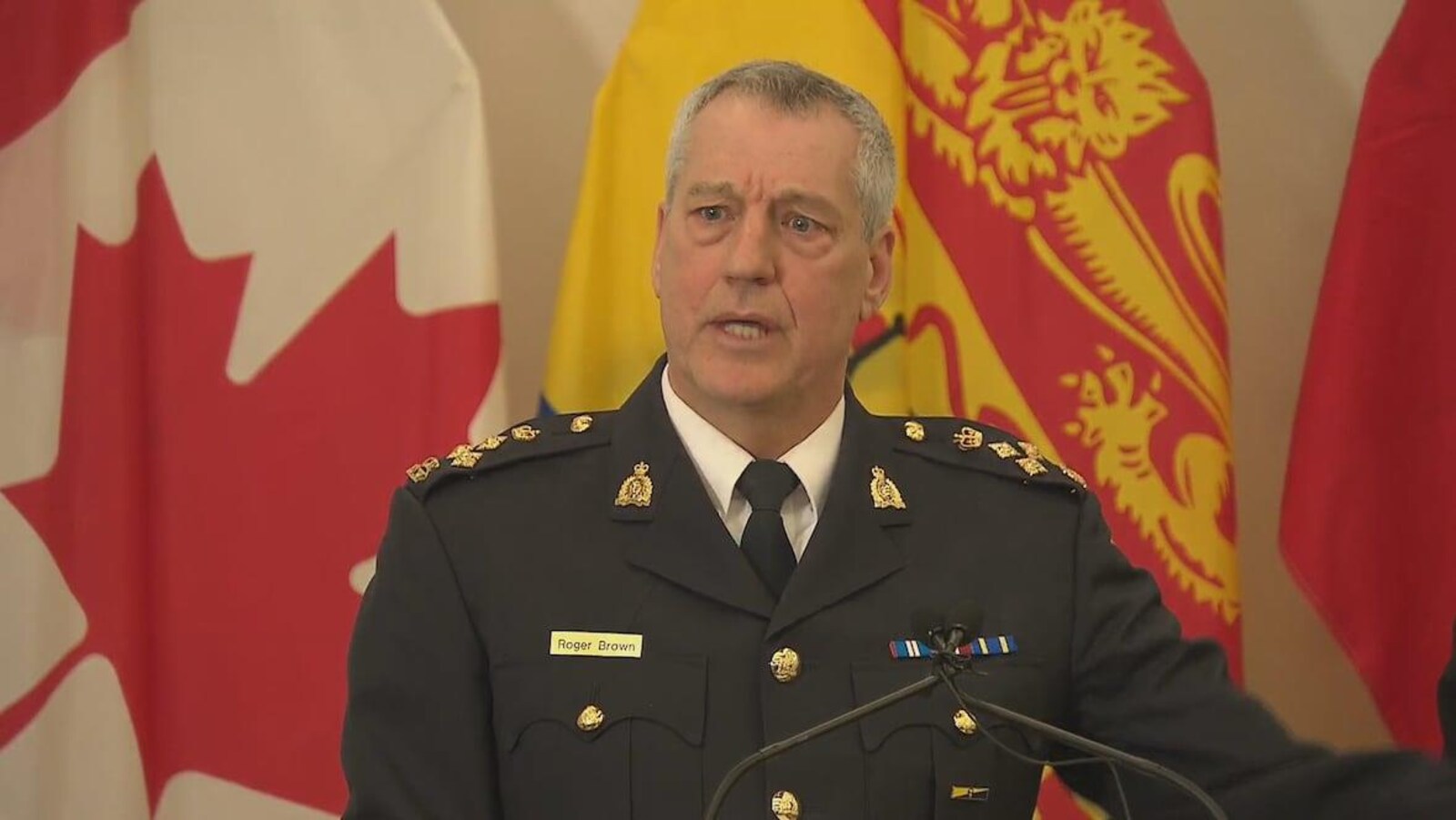 Roger Brown en conférence de presse devant des drapeaux.