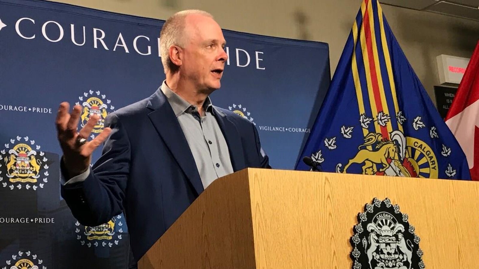 Un homme parle à un podium, avec le drapeau de la police de Calgary en arrière-plan.
