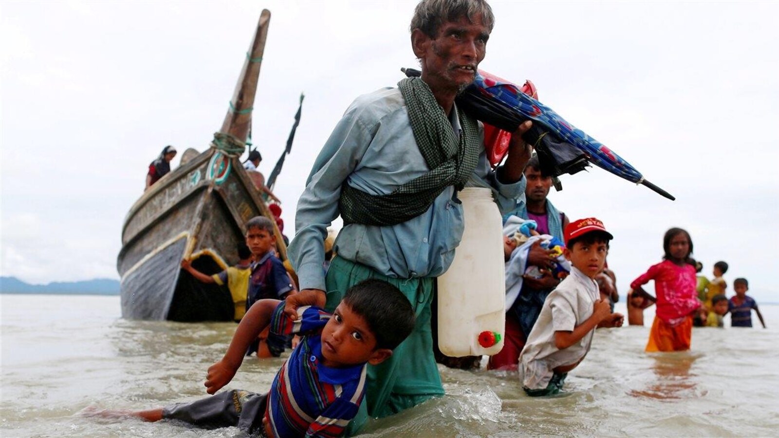 Un réfugié rohingya ayant de l'eau jusqu'aux genoux tire un jeune enfant par le bras.