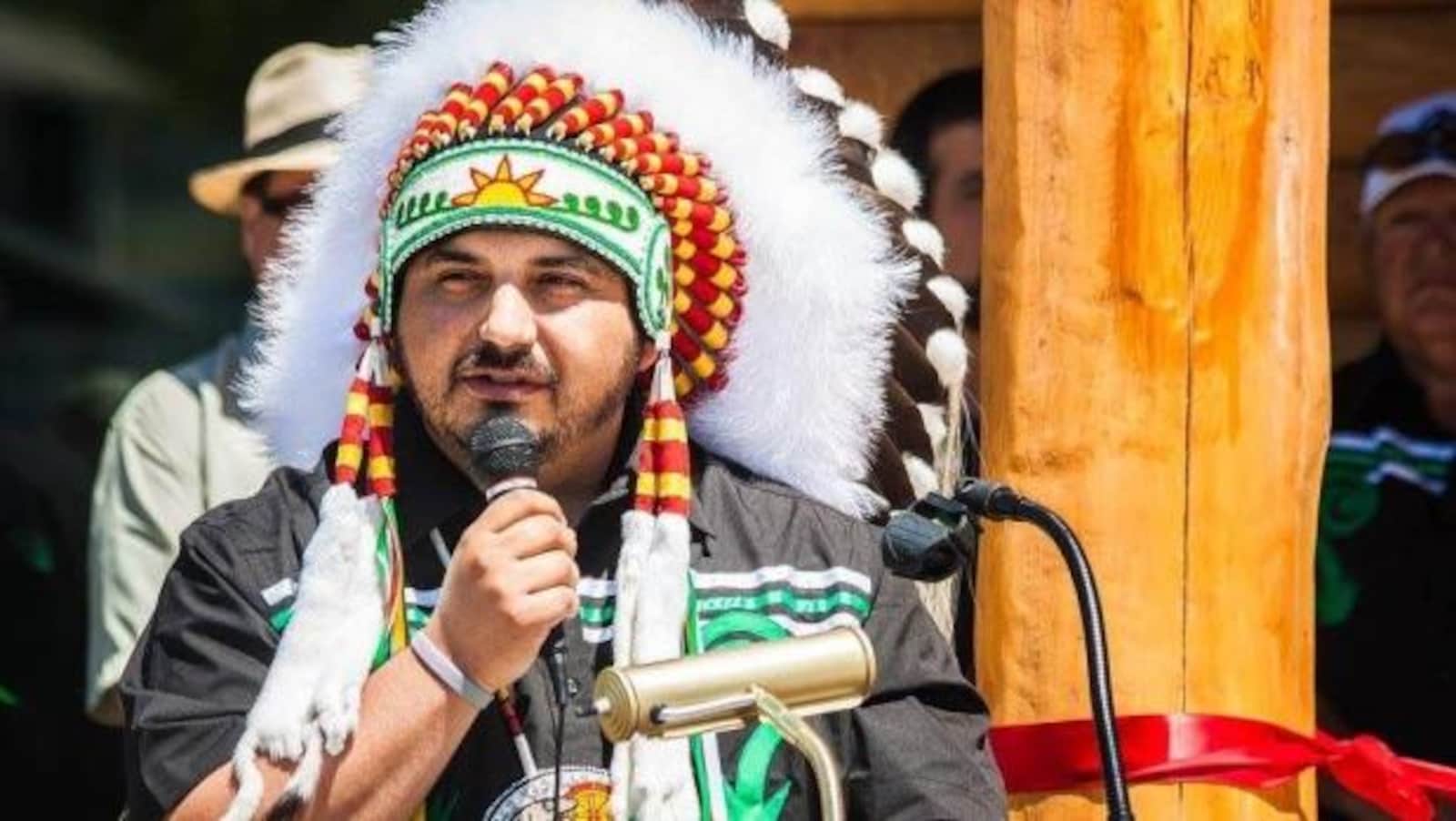 Le chef de la communauté malécite de Tobique, Ross Perley, portant une coiffe traditionnelle, au micro lors d'un rassemblement à l'extérieur