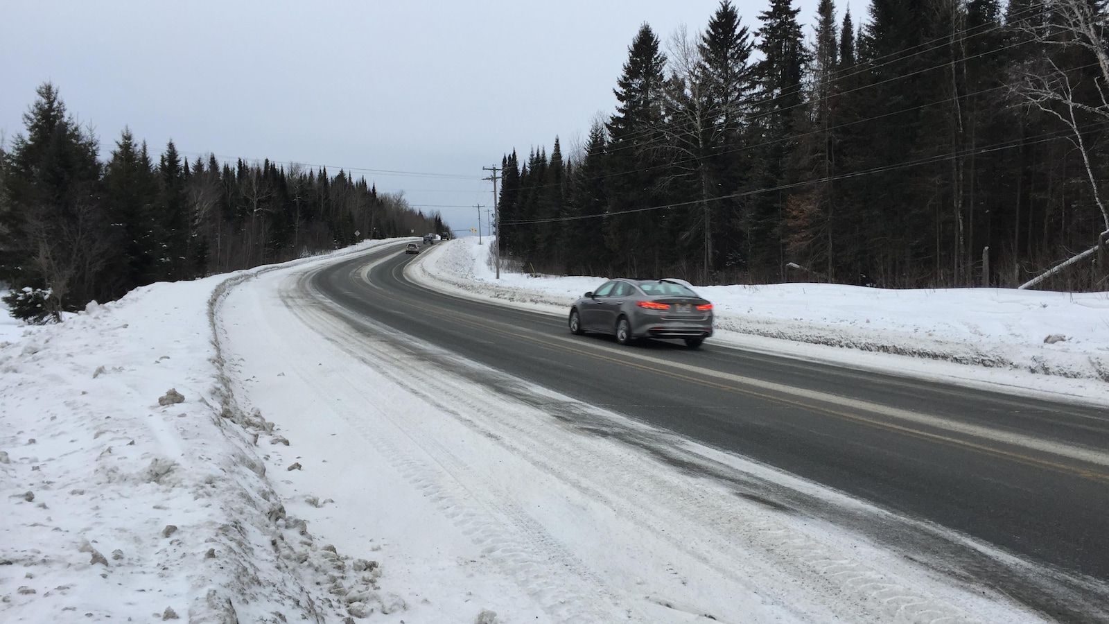 Une voiture roule sur une route enneigée.