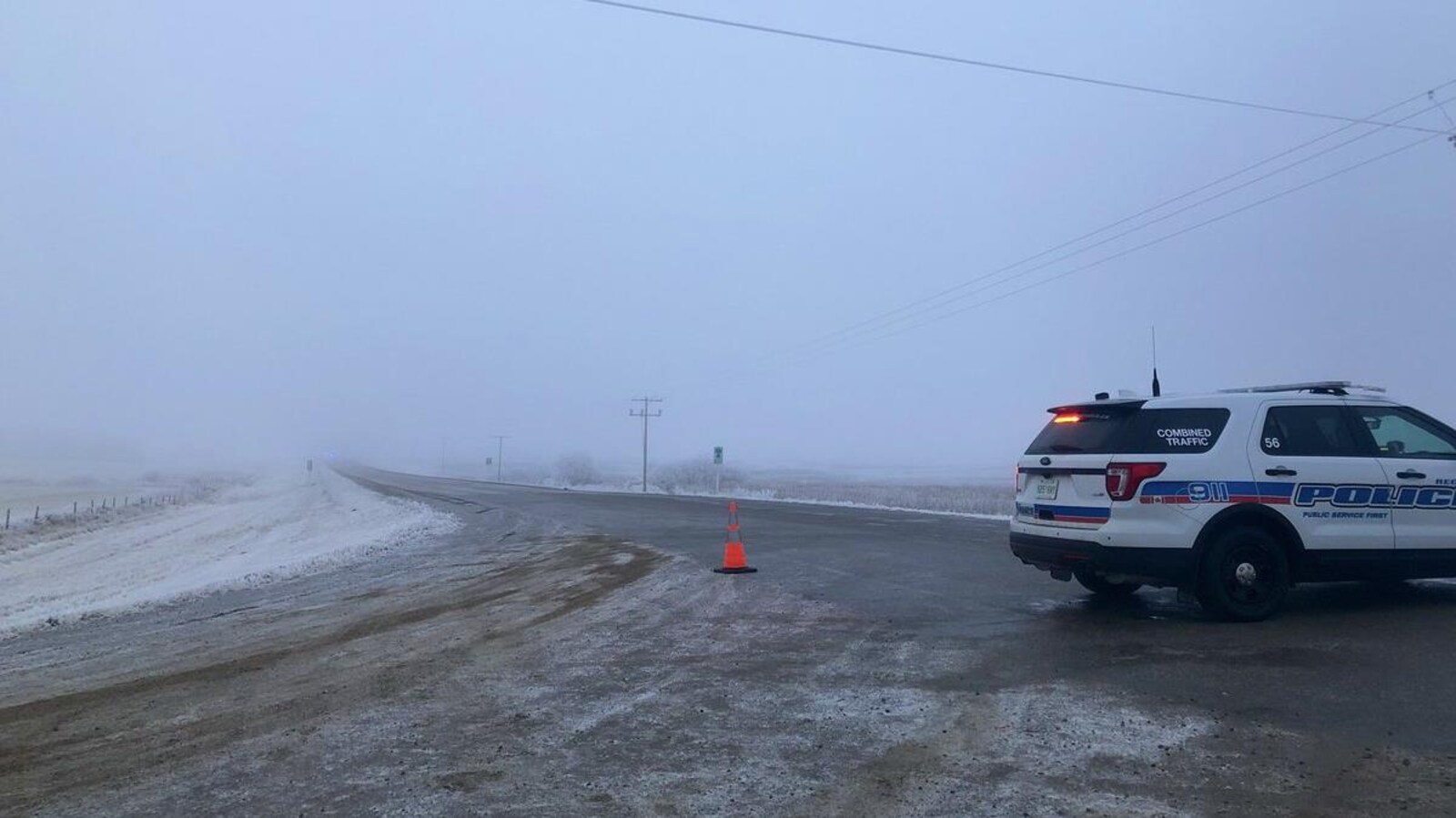 Un véhicule de police bloque une route de campagne nappée de brouillard en Saskatchewan.