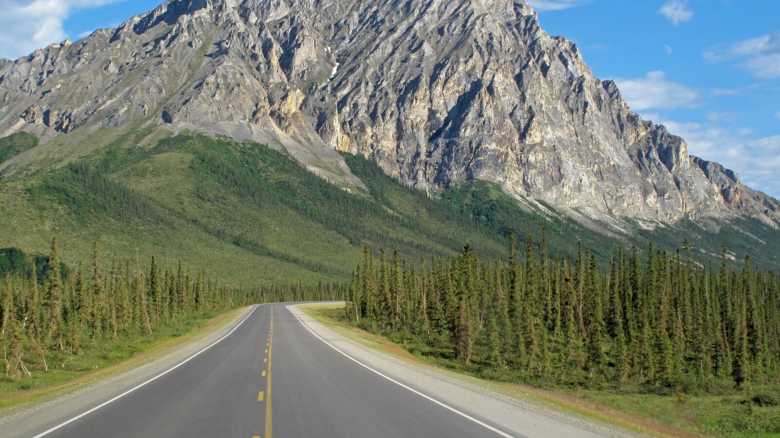 Une route dans la forêt et une grande montagne rocheuse en arrière-plan.