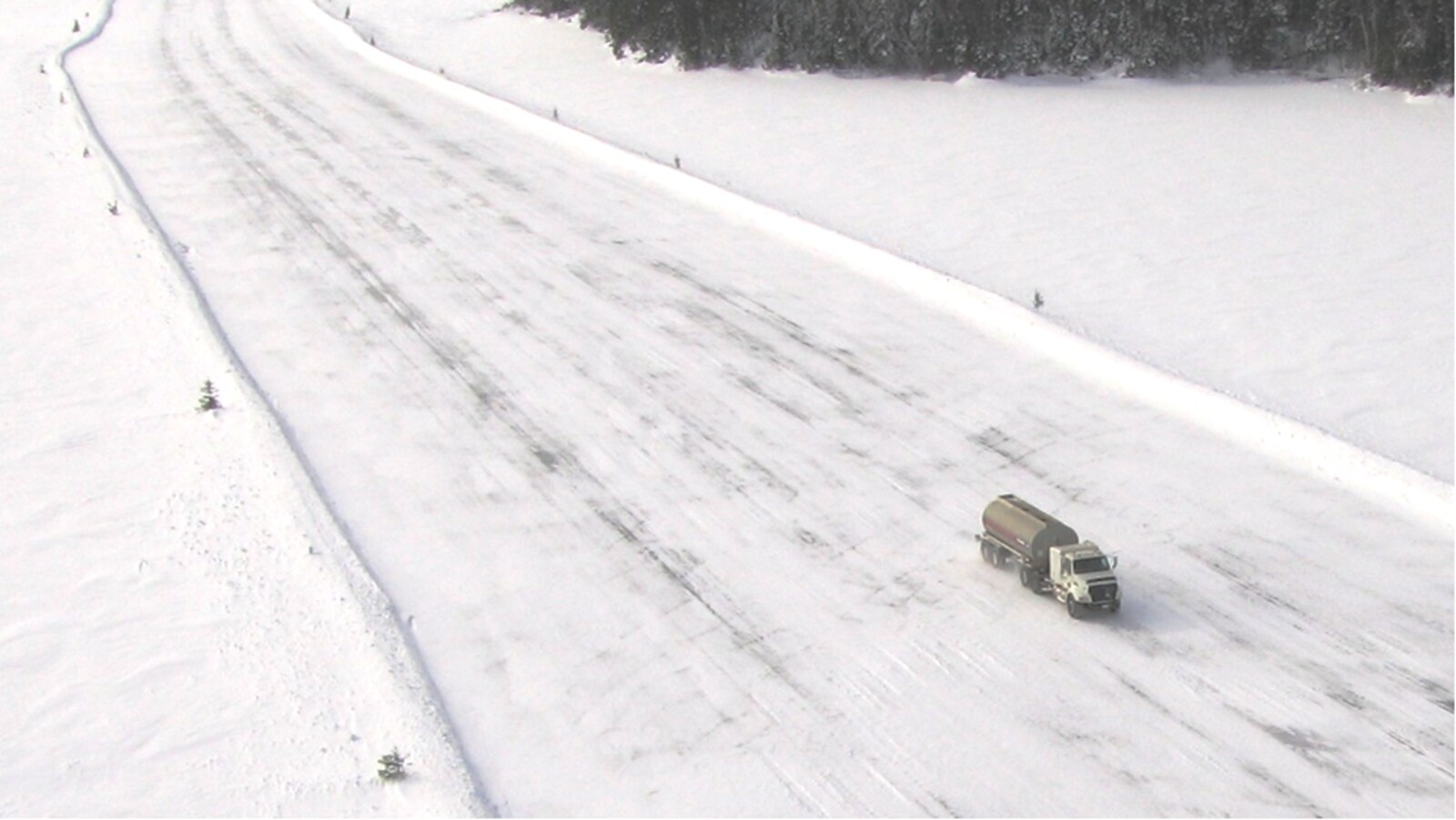 Un camion-citerne circule sur une route de neige et de glace au milieu au milieu d'une grande étendue de neige et de sapins.