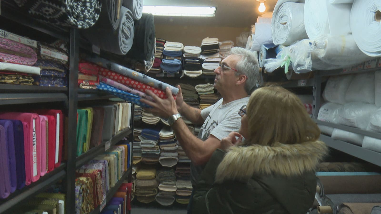 Paul Roy prend des rouleaux de tissus d'une étagère pour les montrer à une cliente.