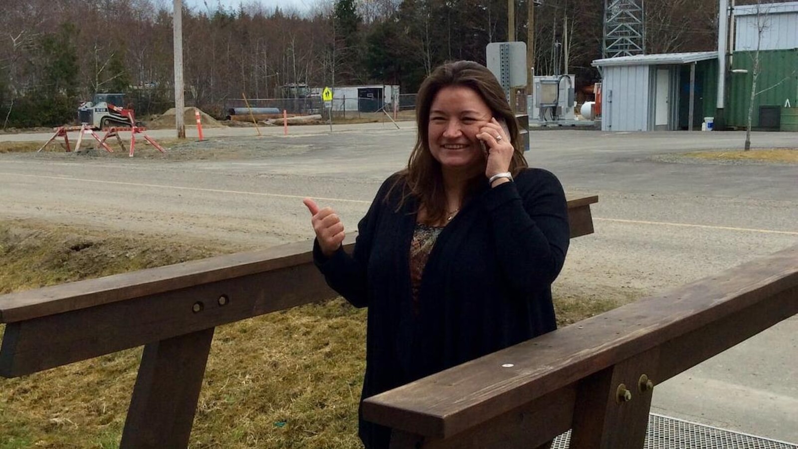 Une femme discute au téléphone en souriant au pied d'une tour métallique.