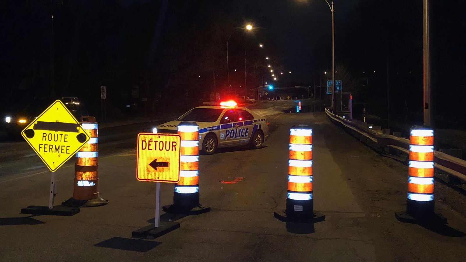 Des cônes orange et une voiture de police bloquent une rue.