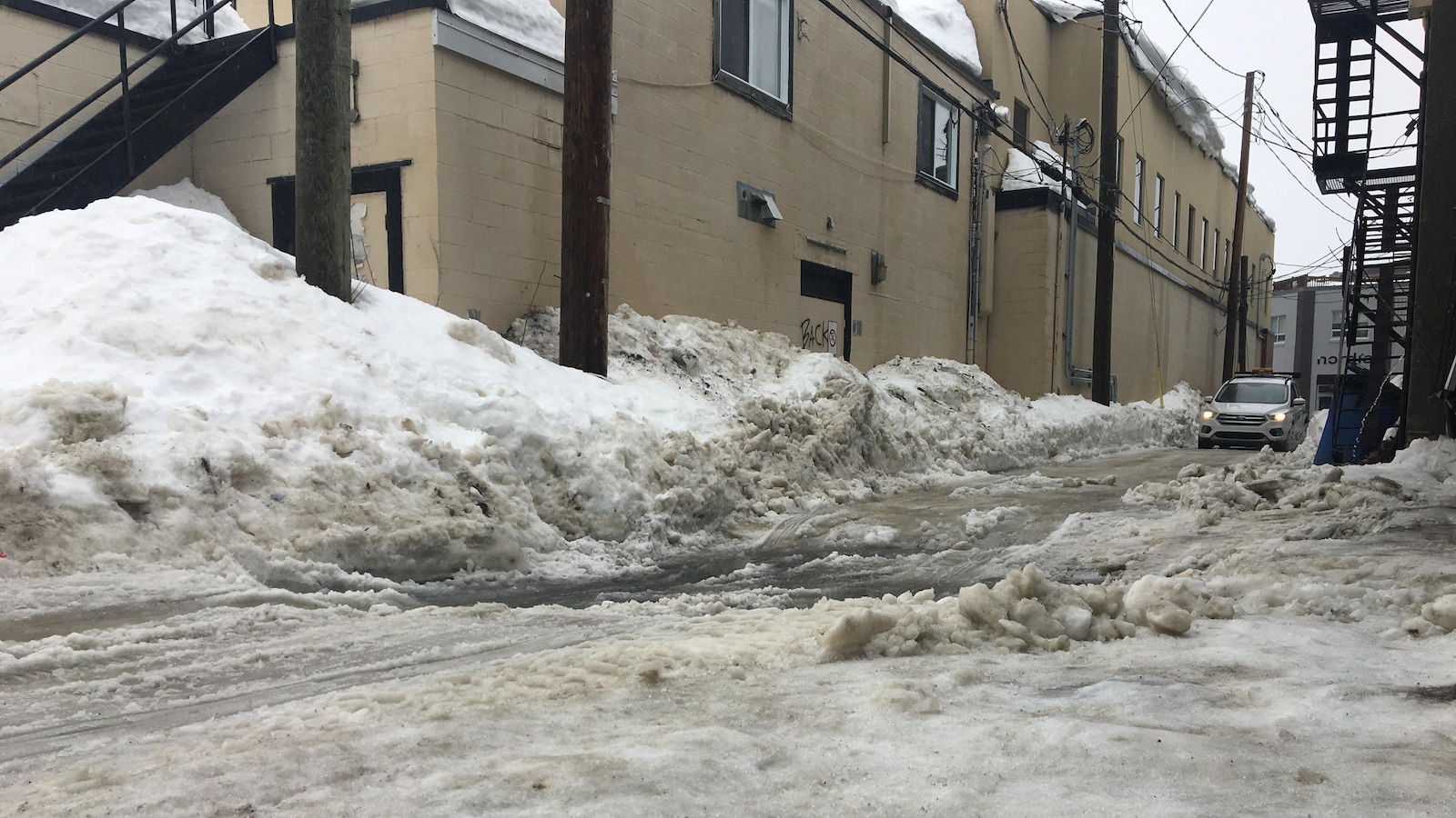 Une voiture circule dans une ruelle où la neige commence à fondre.