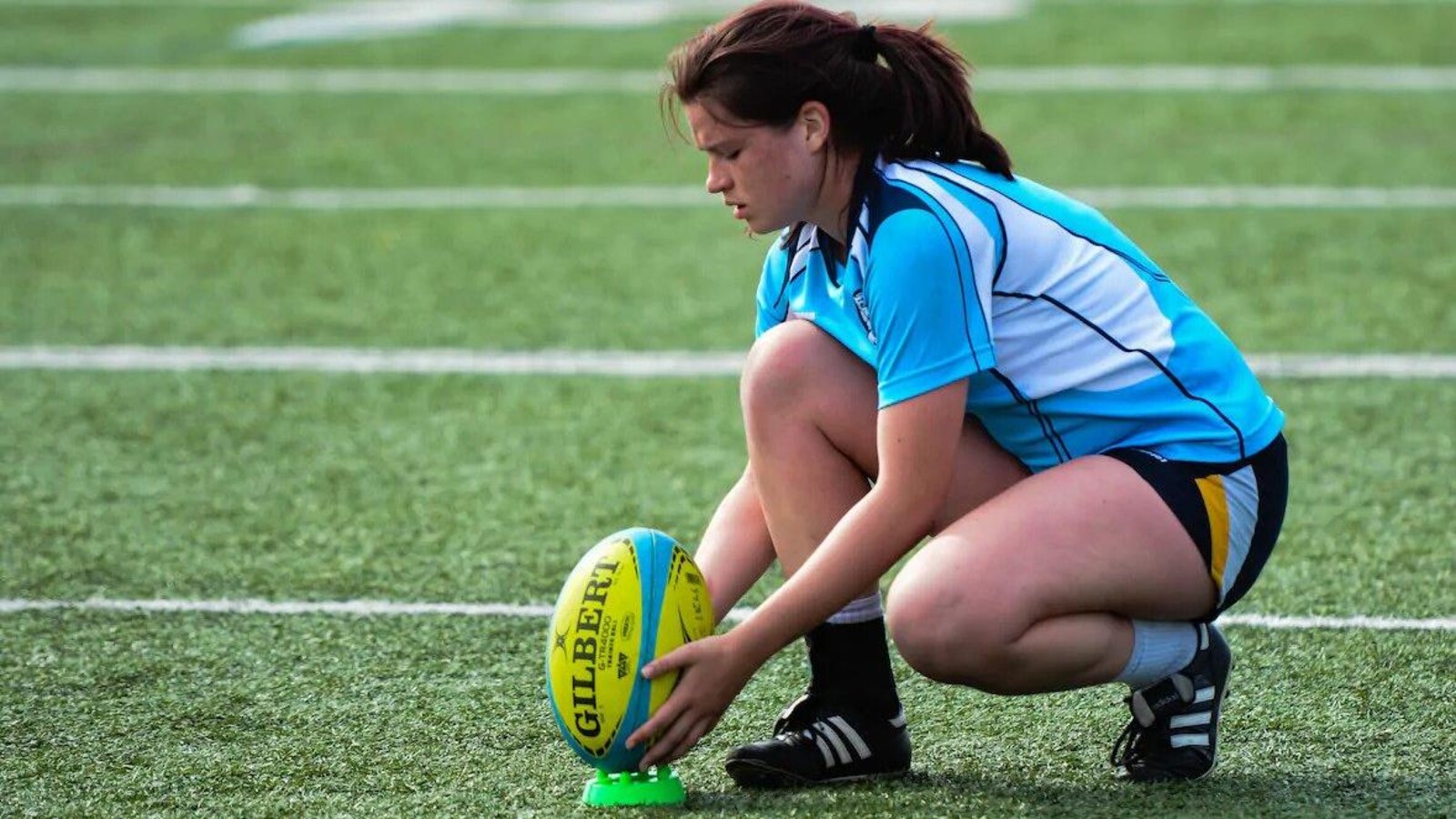 Joueuse de rugby agenouillée devant le ballon.