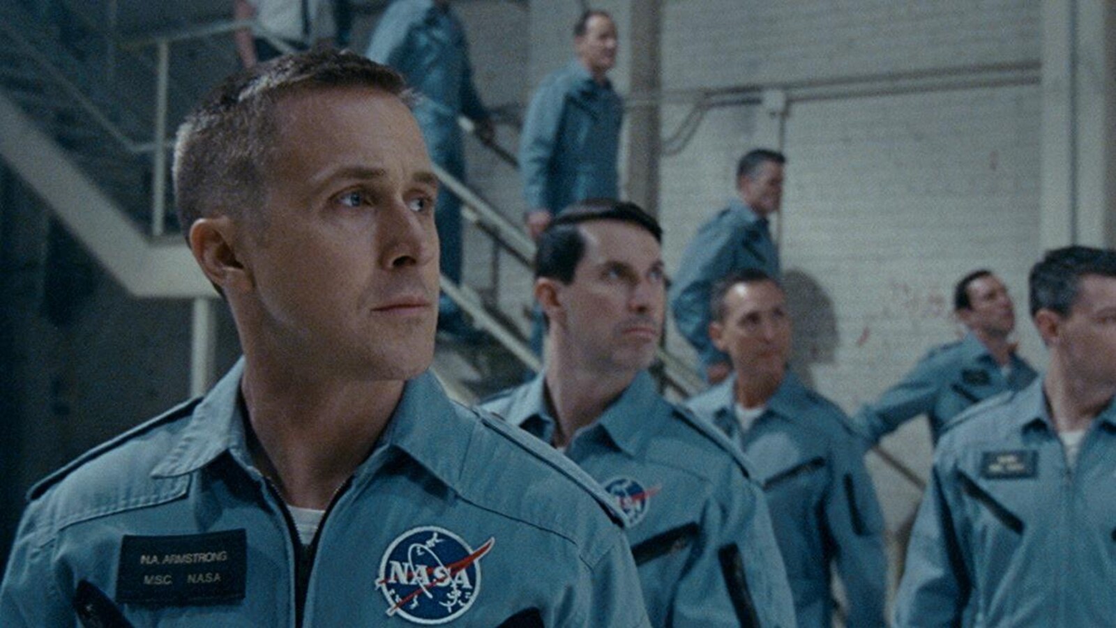 Ryan Gosling, en uniforme de la NASA, regarde vers la droite, tout comme d'autres astronautes derrière lui.