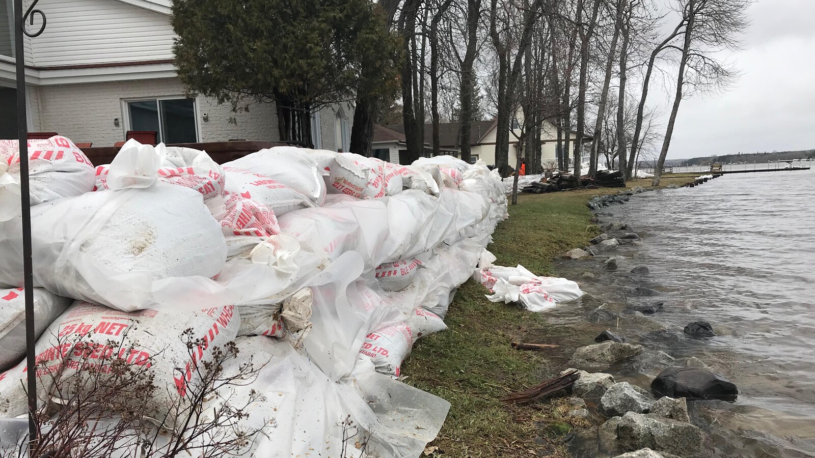 Des sacs de sable sont empilés aux abords d'un lac près de résidences.