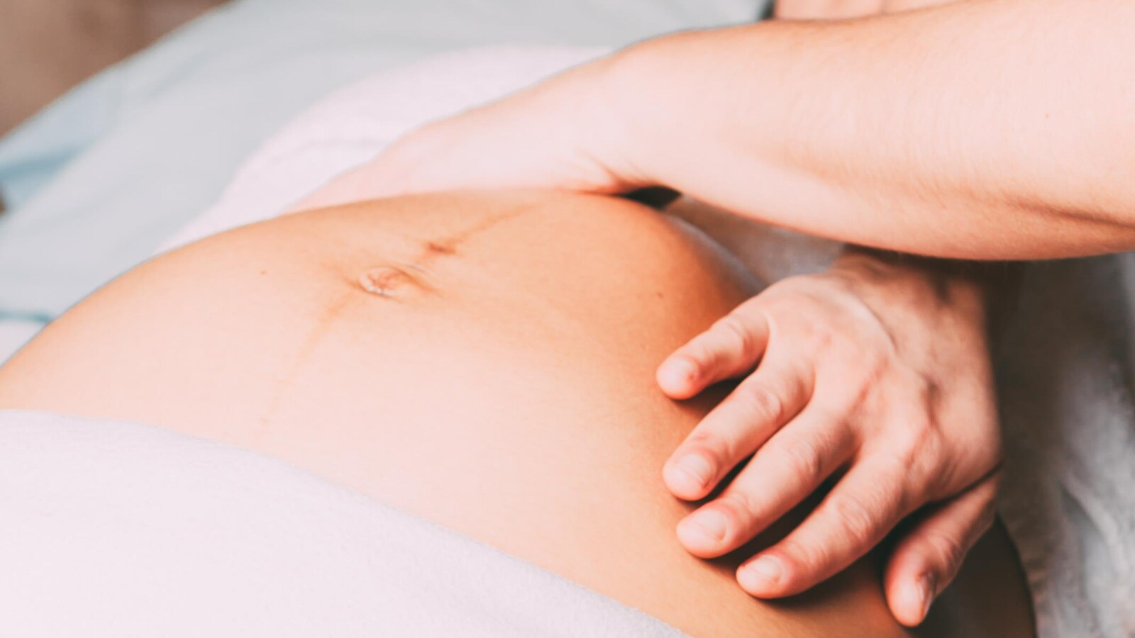 Deux mains de femme sur le ventre d'une femme enceinte couchée sur le dos.