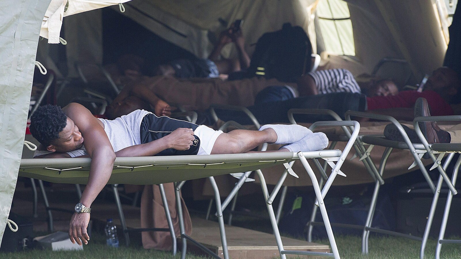 Des réfugiés couchés sur des lits de camp sous une tente.