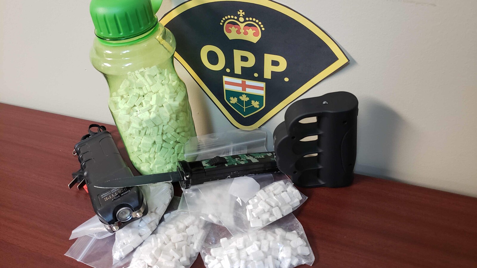 Des sachets de drogue et des armes blanches disposés devant un logo de la PPO.