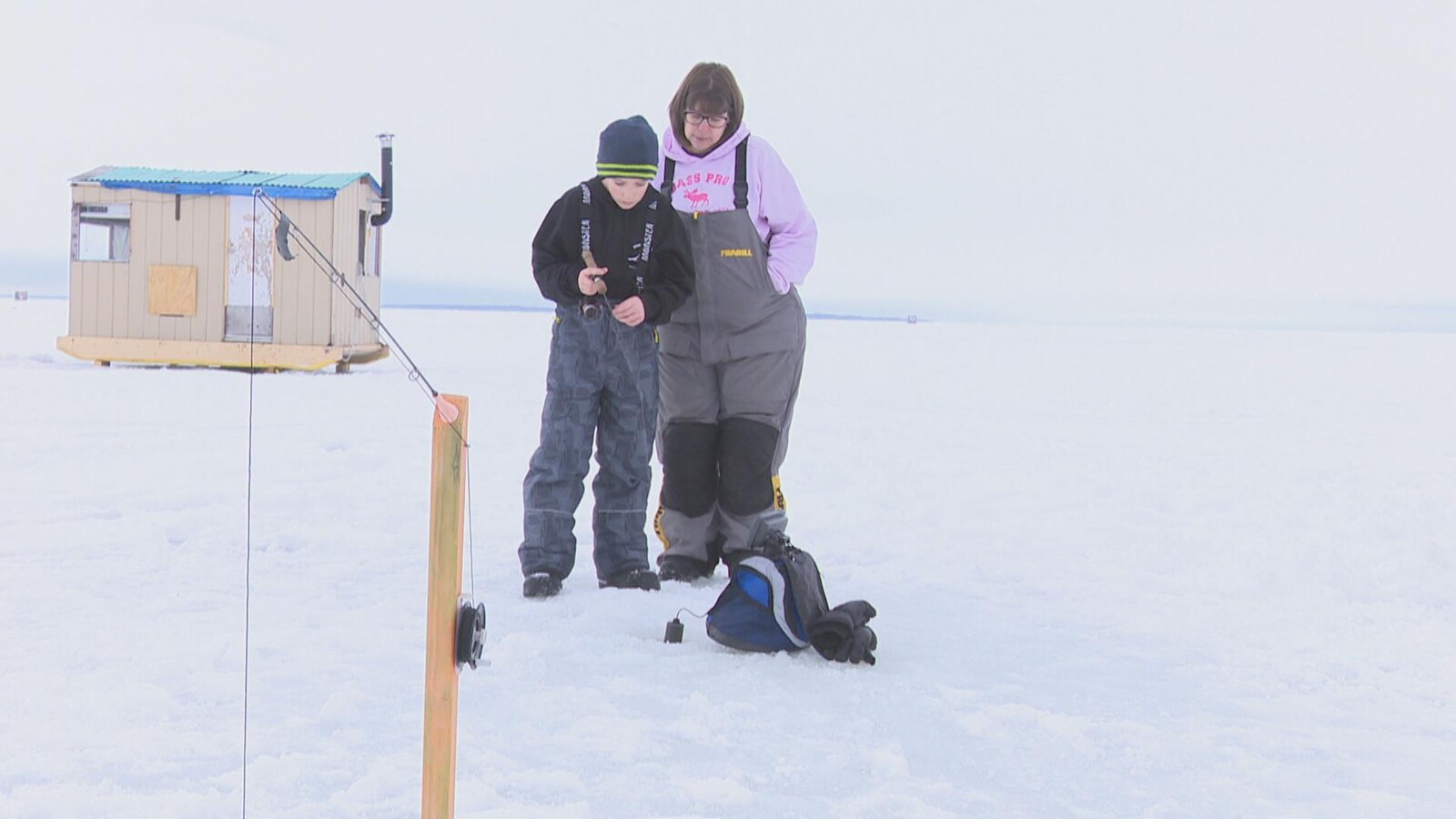 Un jeune garçon et une femme pêchent sur un lac en hiver