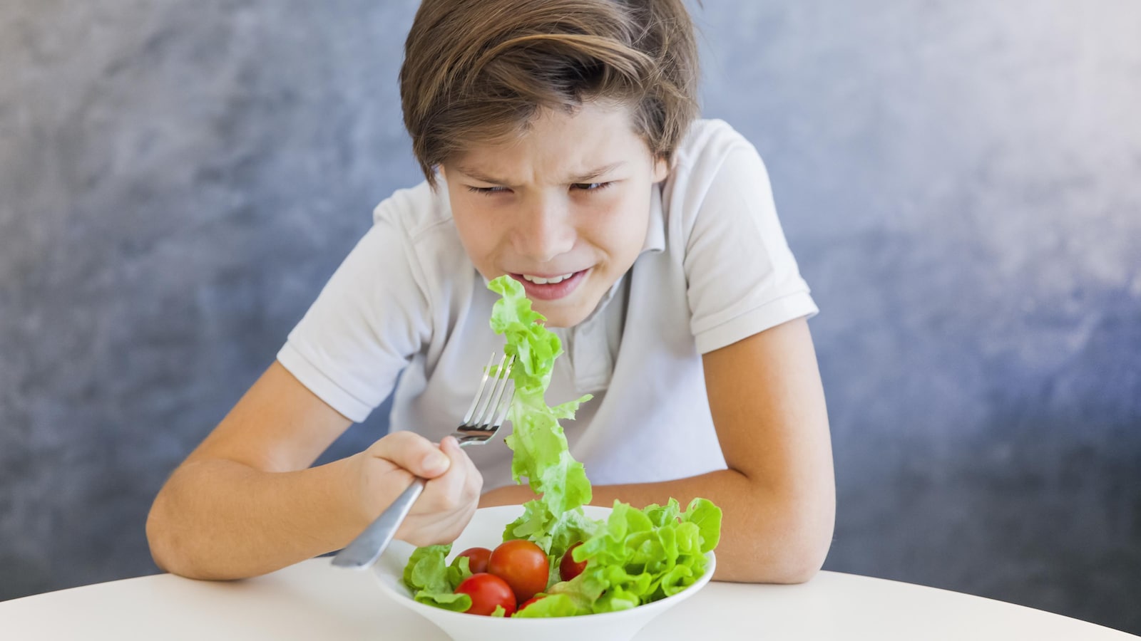 Un garçon d'environ 12 ans grimace devant une salade.
