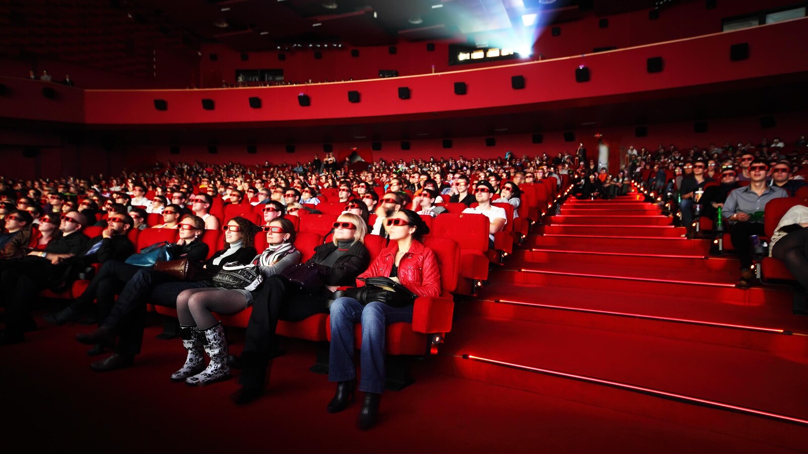 les gens sont assis dans des sièges rouges et portent des lunettes.