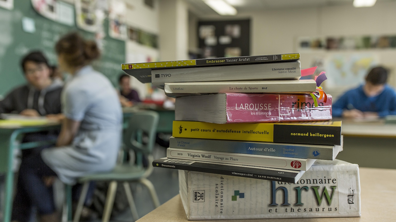 Plusieurs livres empilés dans une classe avec en arrière-plan des élèves.