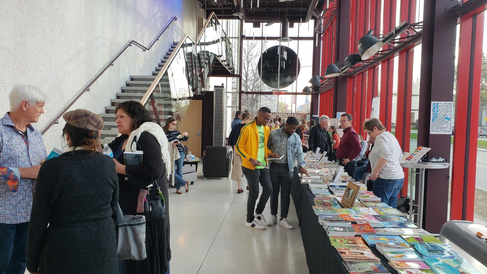 Un stand de livres et des lecteurs dans l'entrée du Théâtre Cercle Miolière de Winnipeg.