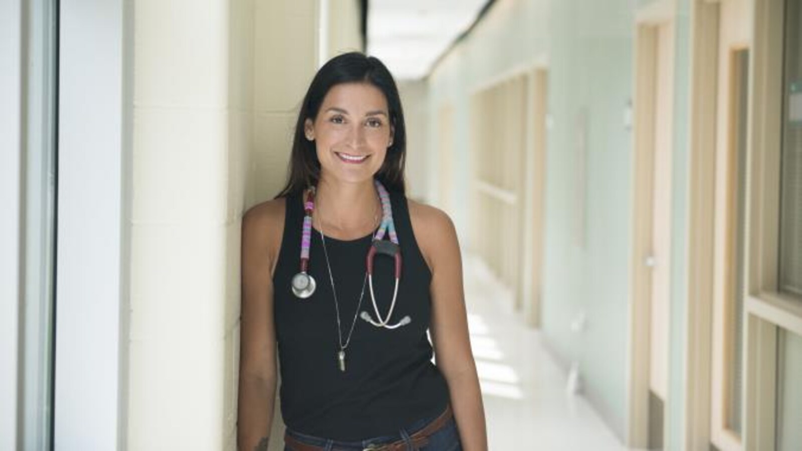 Portrait d'une femme dans un corridot. Elle porte un stéthoscope autour du cou.