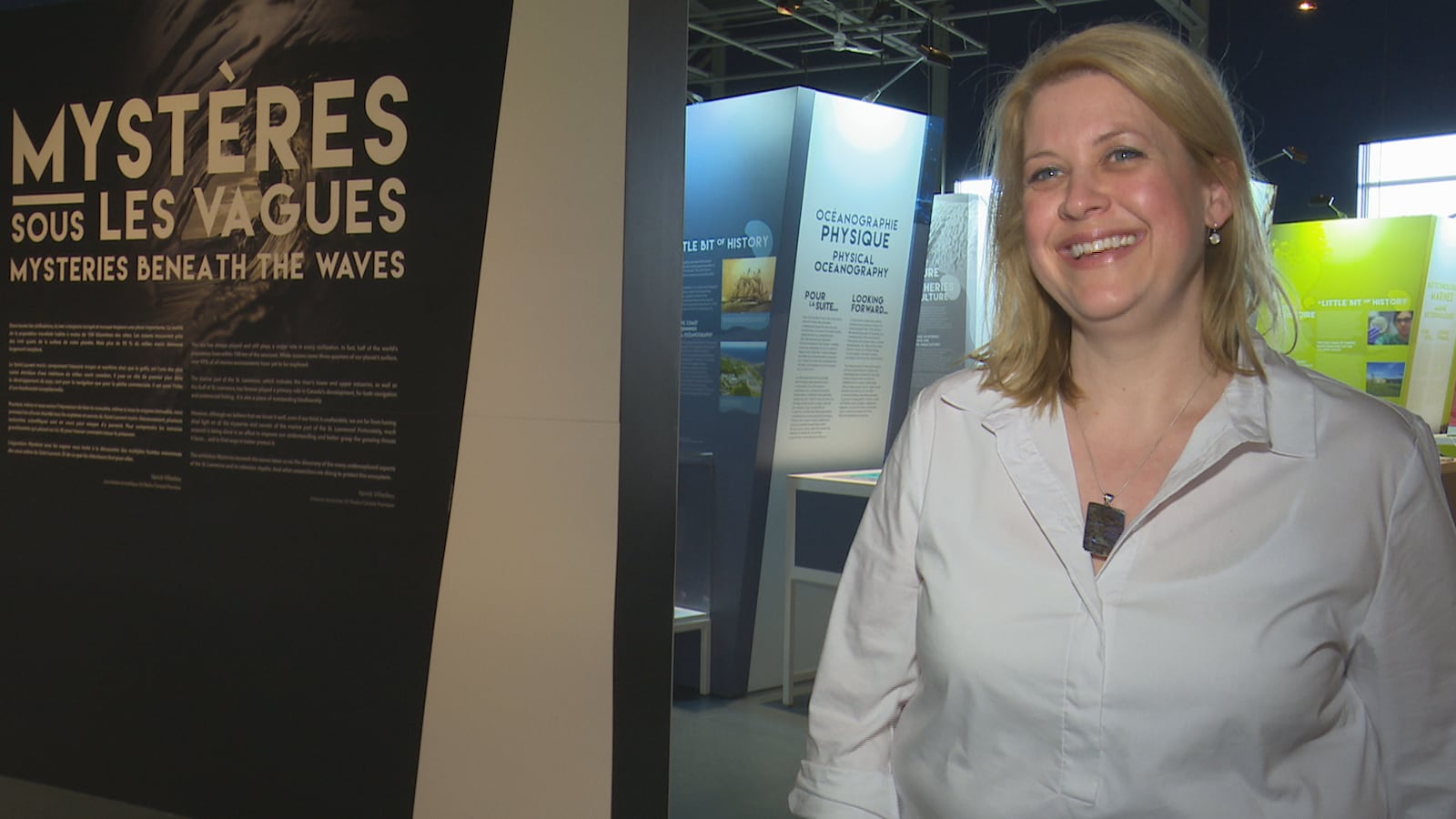 La directrice sourit devant une salle d'exposition du musée.
