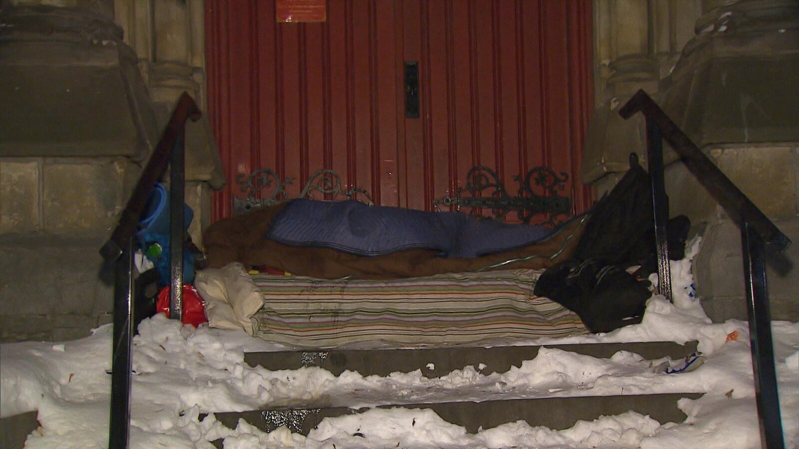 Couchette improvisée dans la neige, au haut d'un escalier, devant une porte