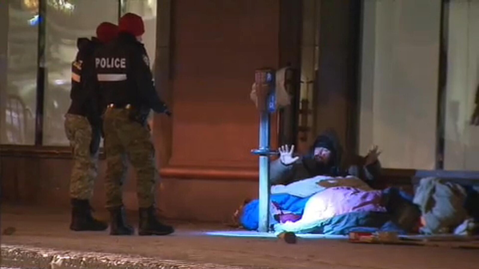 Deux policiers parlent avec un sans-abri qui dort devant un magasin du centre-ville de Montréal
