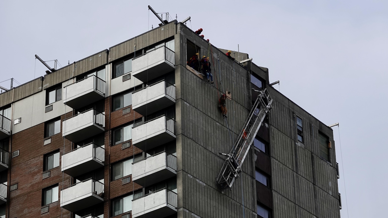 Un travailleur est hissé au moyen de cordages vers une ouverture dans le mur de l'immeuble.