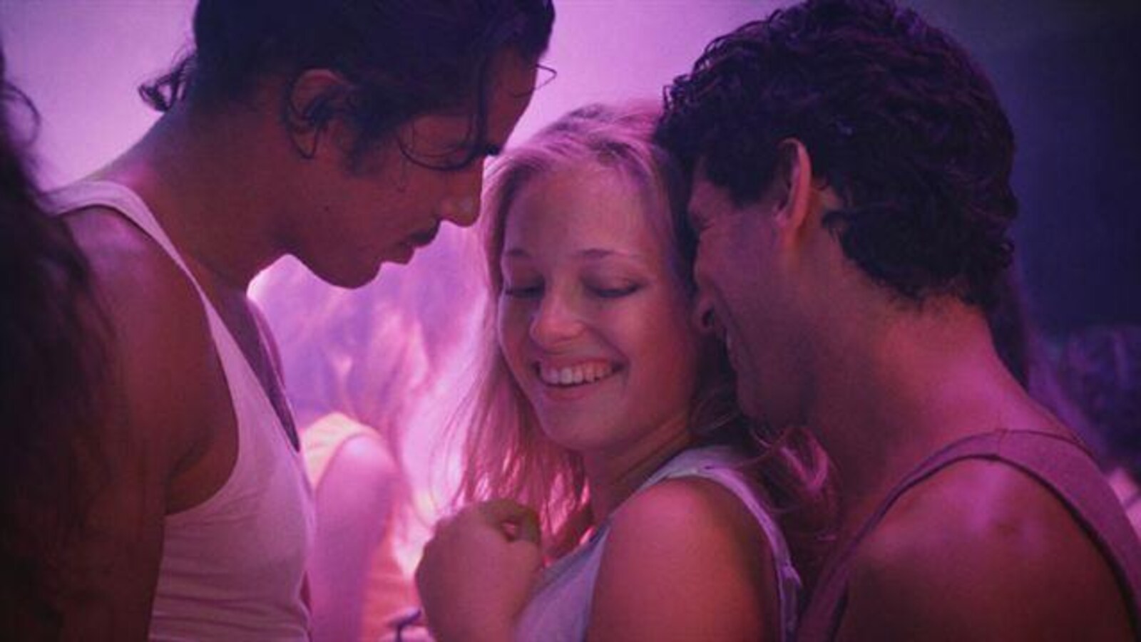 Une femme dans une boîte de nuit danse collée sur deux hommes.