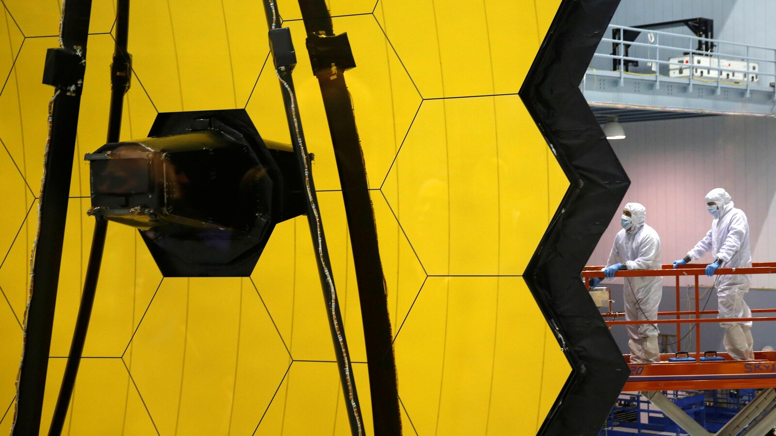 Des travailleurs en combinaison près d'un télescope spatial.