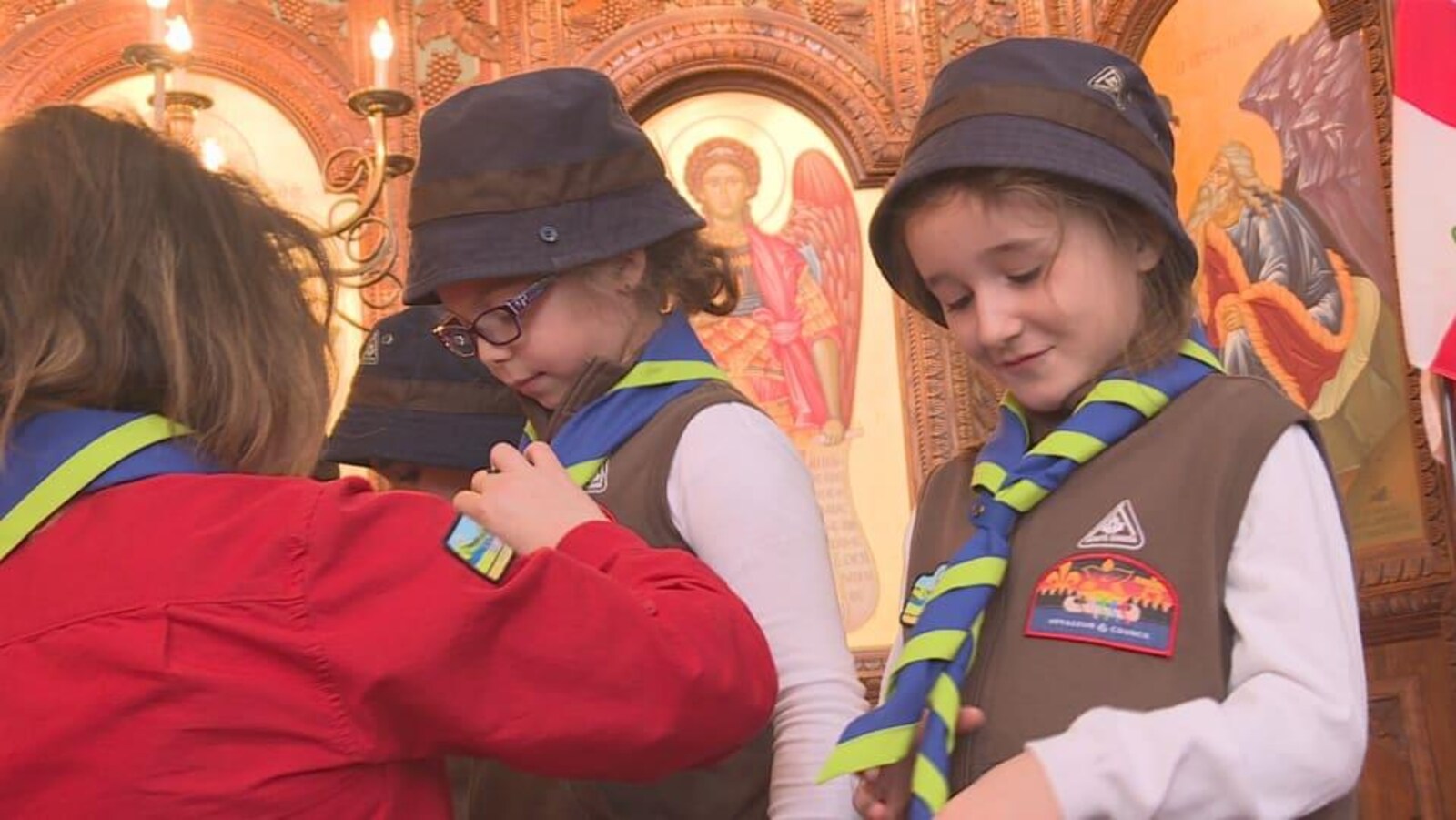 Une fillette en habit de scout regarde fièrement son foulard vert et bleu.
