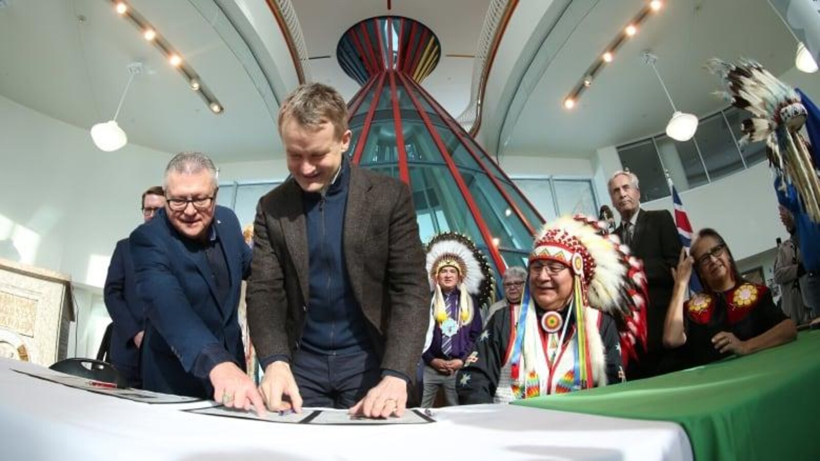 Seamus O’Regan et Ralph Goodale debout regardent un document placé sur une table au bord de laquelle est assis Michael Starr.