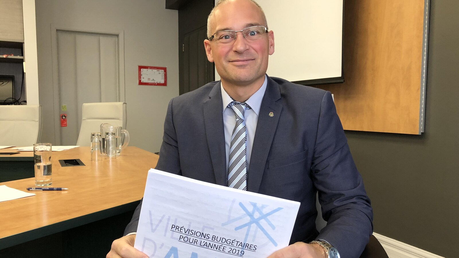 Sébastien D'Astous sourit à la caméra en tenant le document Prévisions budgétaires pour l'année 2019.