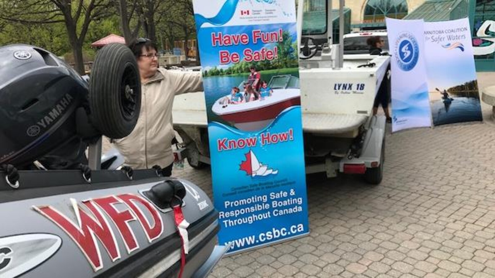 Une femme tient une affiche promouvant les règles de sécurité en bateau, entre deux embarcations de services de secours.