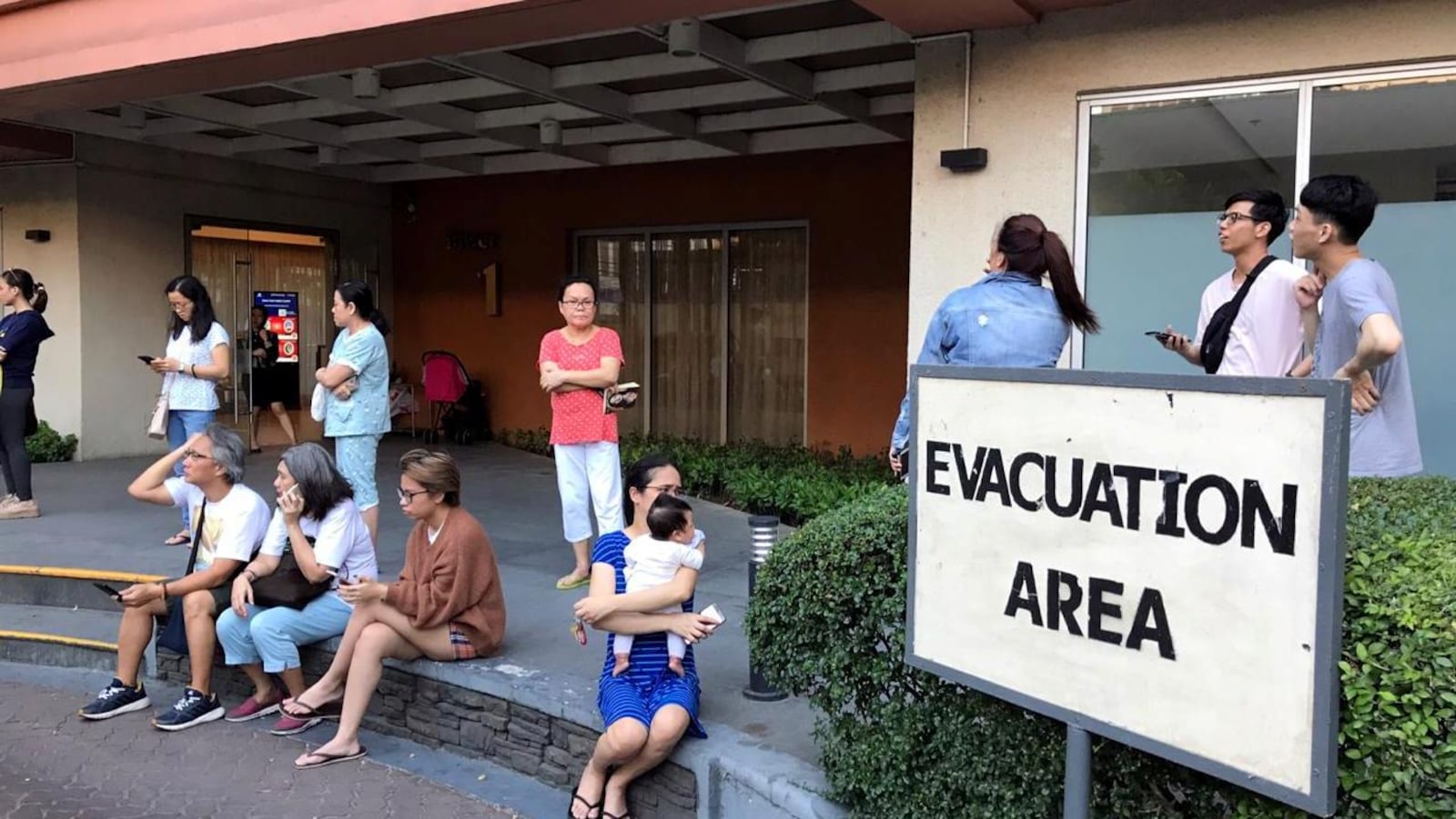 Des gens assis près d'une pancarte : «Zone d'évacuation»