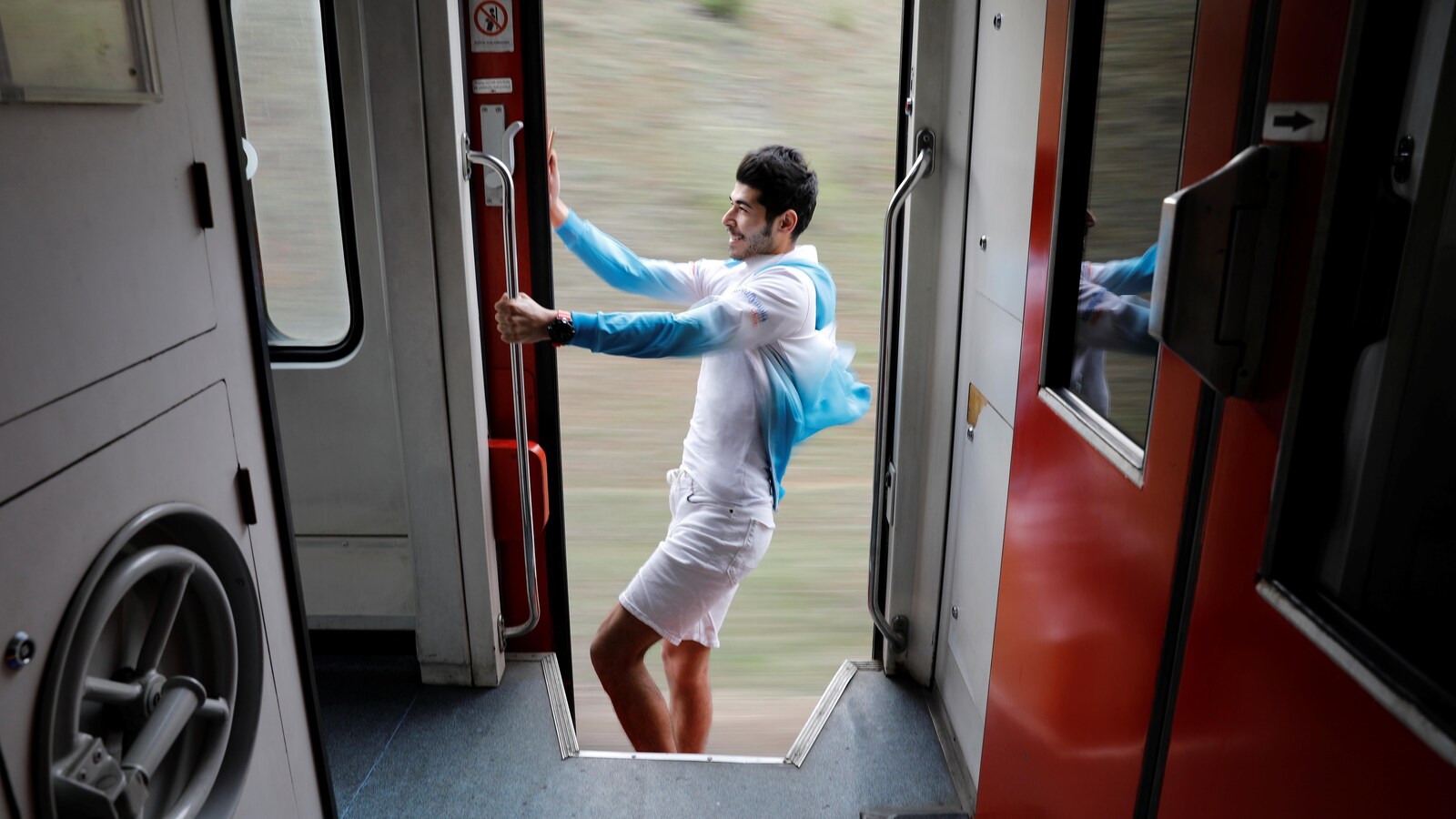 Le jeune homme se tient d'une main à l'extérieur du train en mouvement.