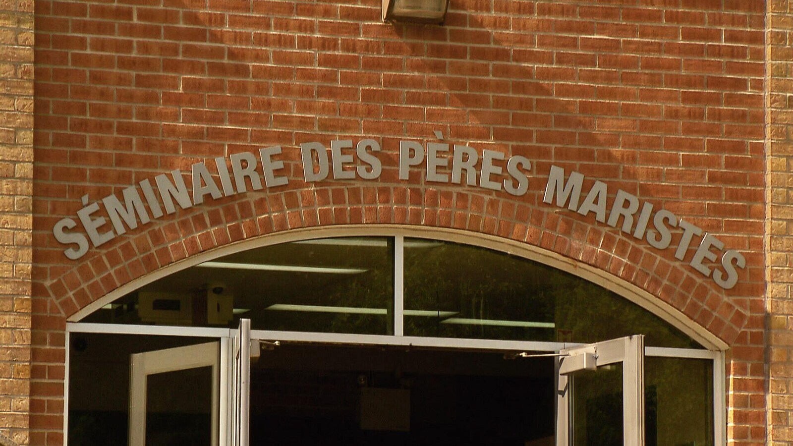 Entrée principale du Séminaire des Pères Maristes. On aperçoit le nom de l’établissement inscrit en lettres grises au-dessus d’une double porte vitrée. La façade de l’édifice est en brique.