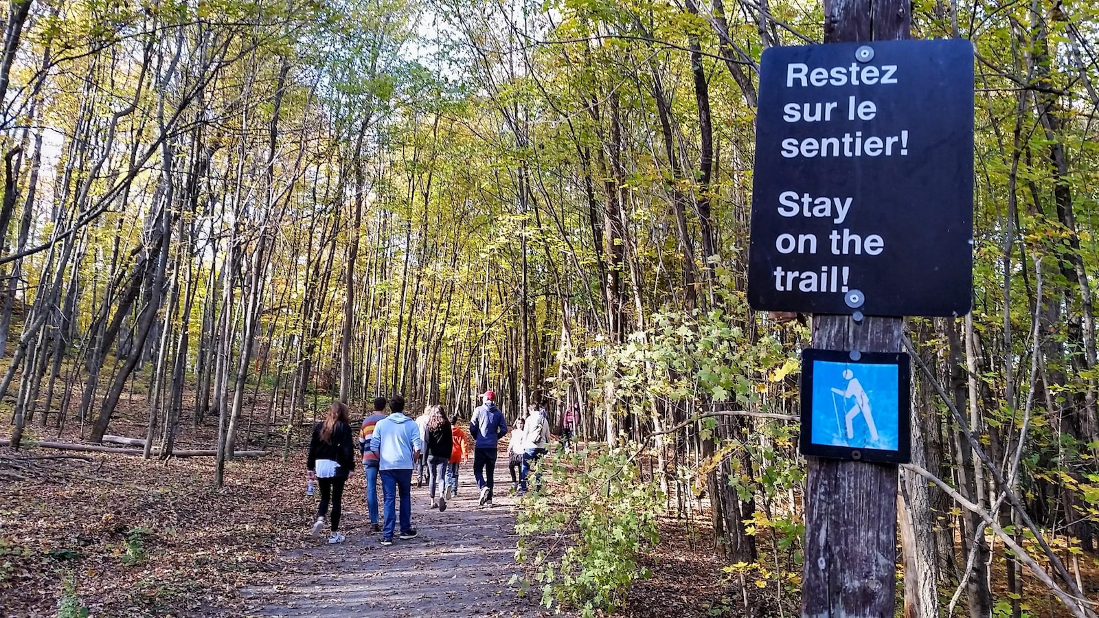 Des randonneurs dans le parc de la Gatineau, à l'automne. Sur une affiche, on peut lire : « Restez sur le sentier! » (Archives)
