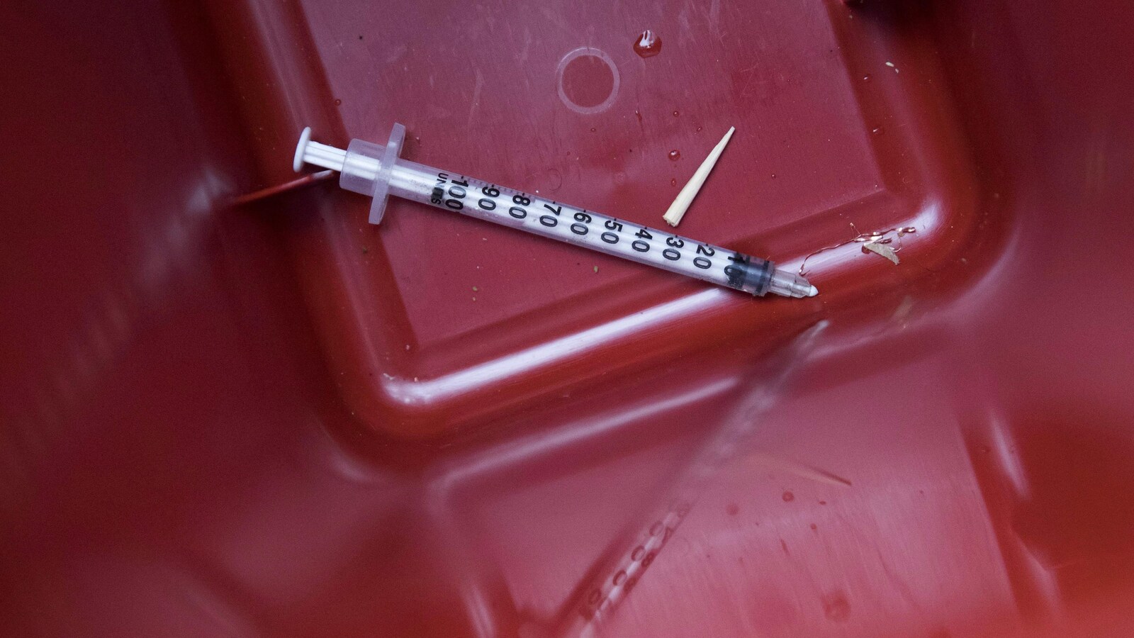Gros plan sur une seringue cassée avec reflet dans un bac rouge.